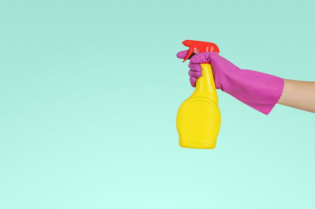 Hand in purple cleaning gloves holding a cleaning bottle